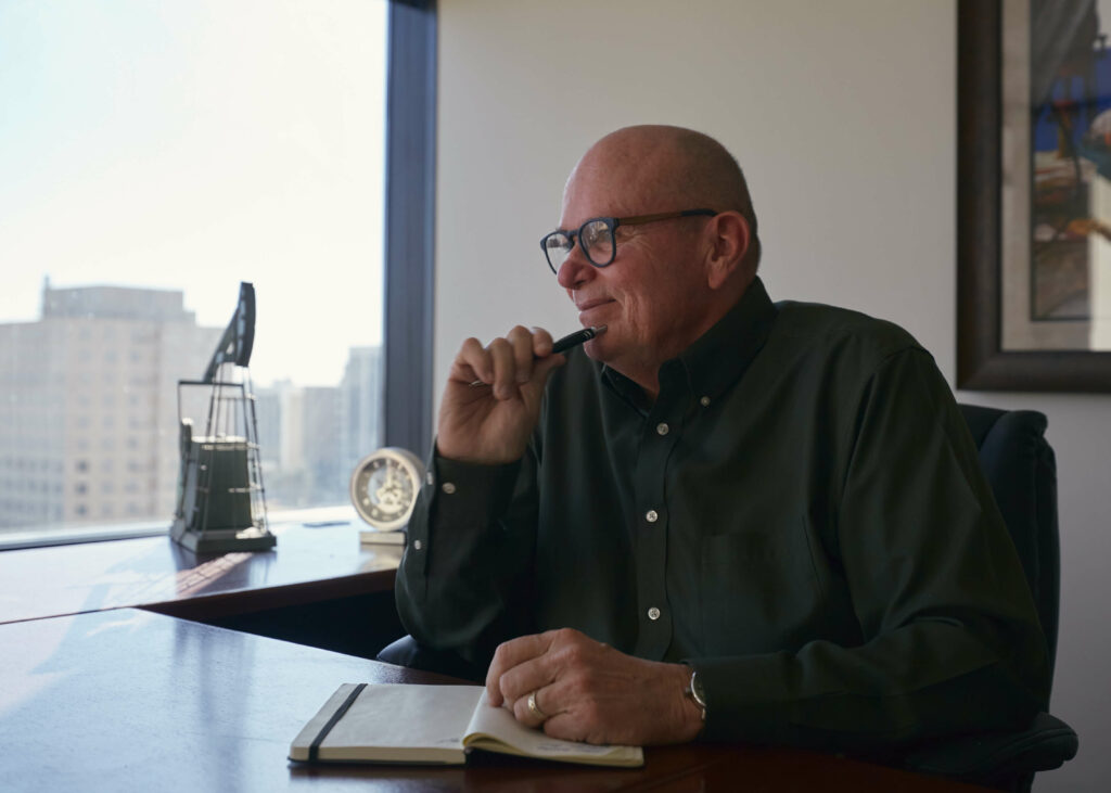 Roy Jackson in a professional office setting, pensively holding a pen, showcasing readiness and willingness to assist businesses in consulting and management.